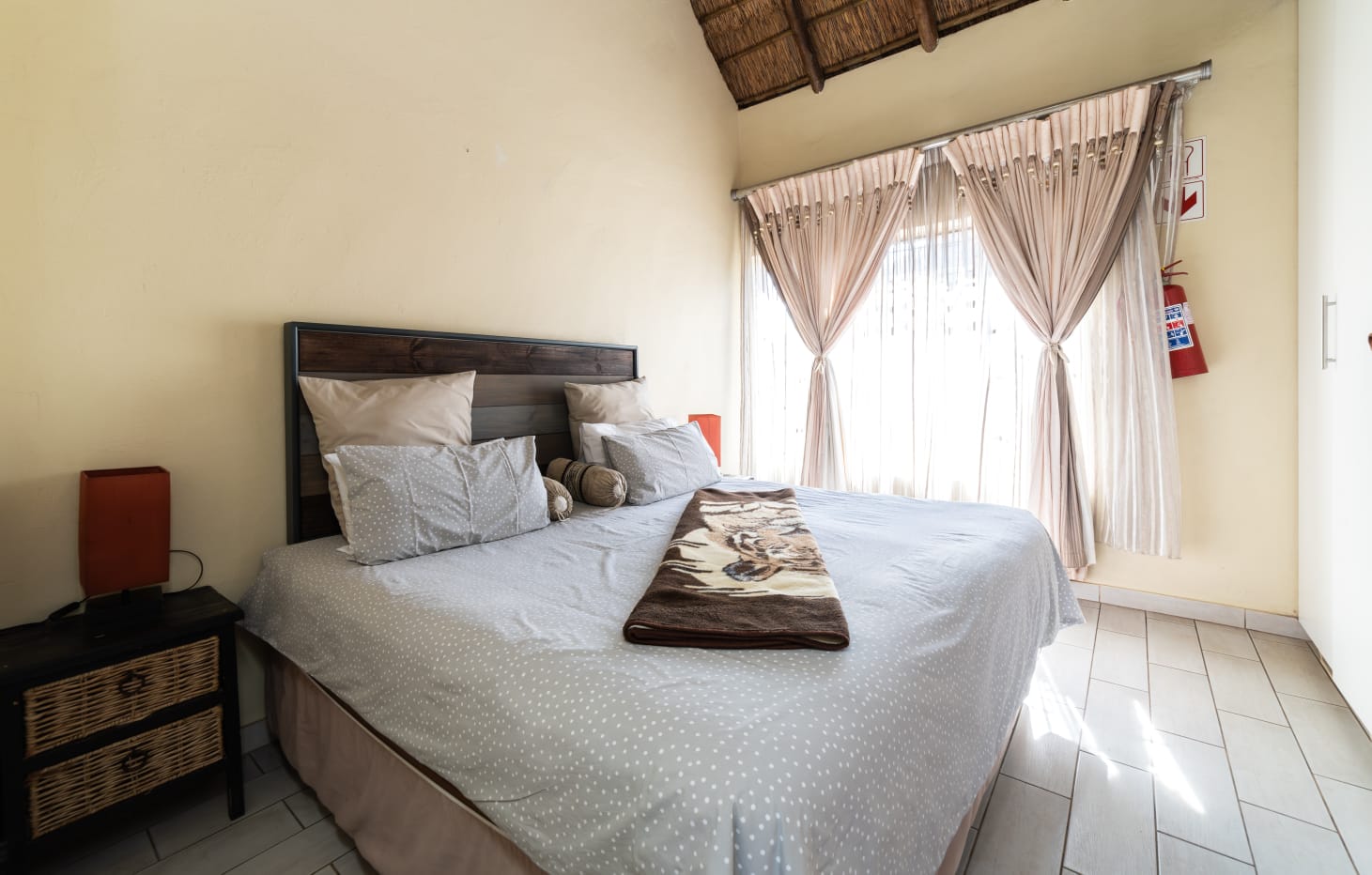 Luxury guest bedroom featuring a high thatch roof, queen-sized bed with African wildlife throw, and elegant drapes.
