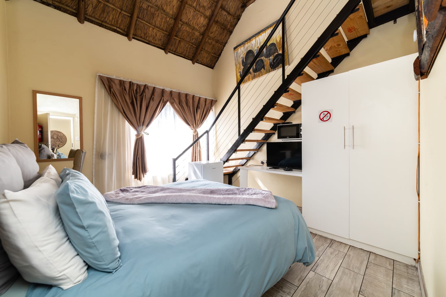 Luxury guest bedroom featuring a high thatch roof, queen-sized bed with African wildlife throw, and elegant drapes.