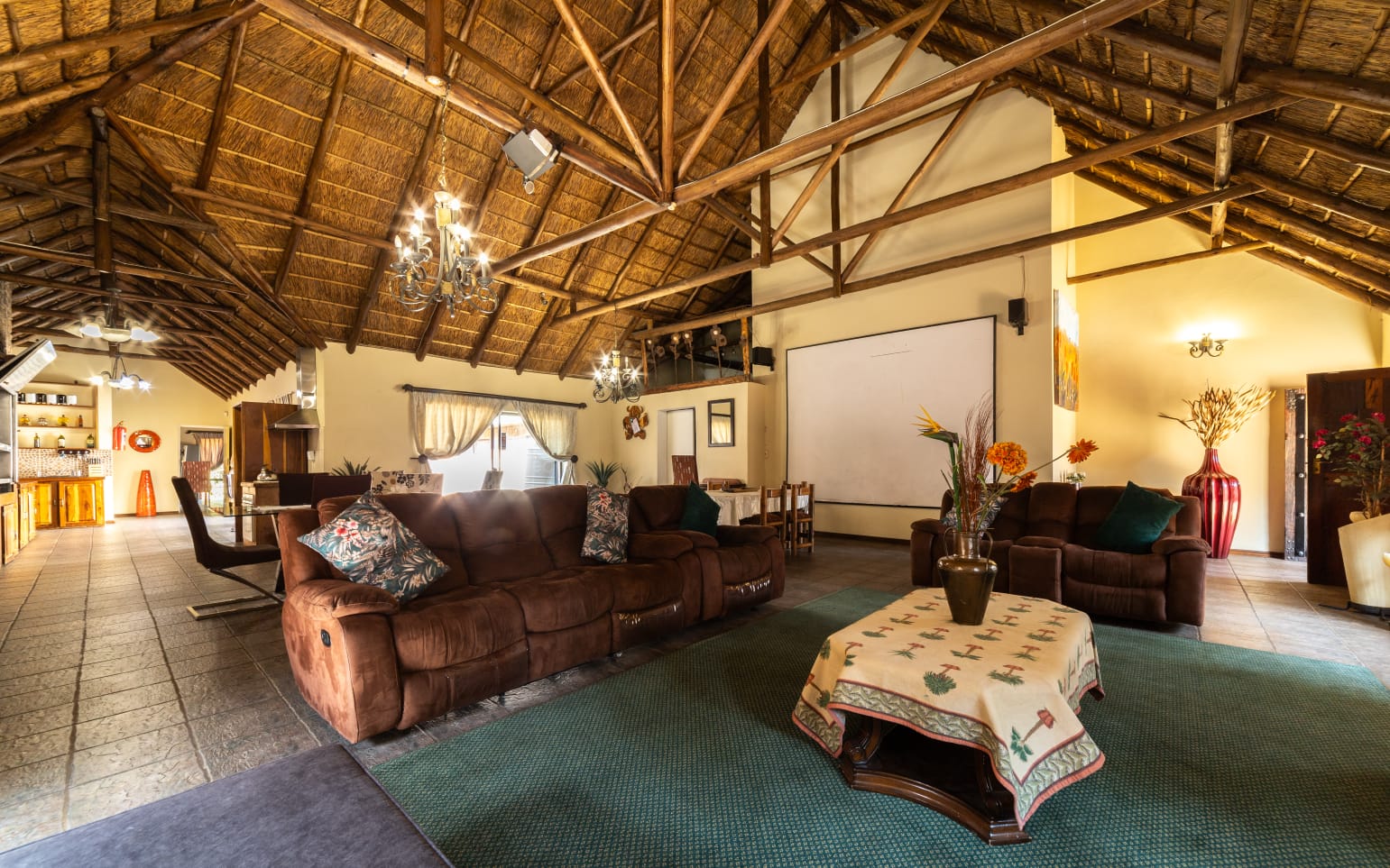 pacious and cozy communal lounge at Thatch Haven with comfortable brown sofas, high thatch ceilings, and warm lighting.
