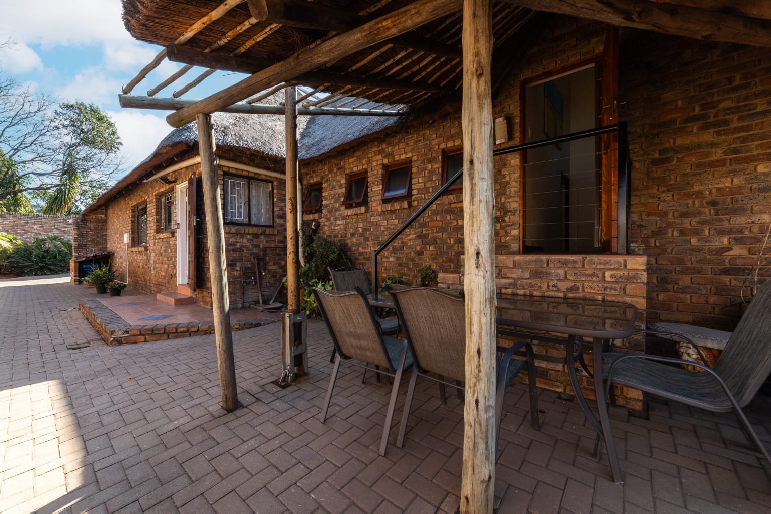 Paved walkway alongside the rustic brick exterior of the guesthouse under a clear blue sky.