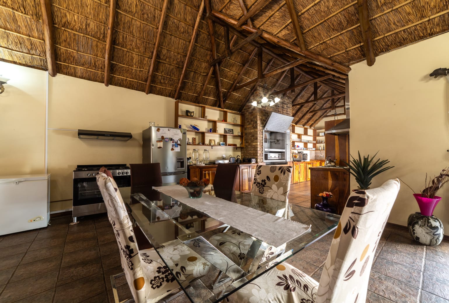 Modern glass dining table in a thatch-roofed dining room, perfect for guest breakfasts at our Centurion accommodation.