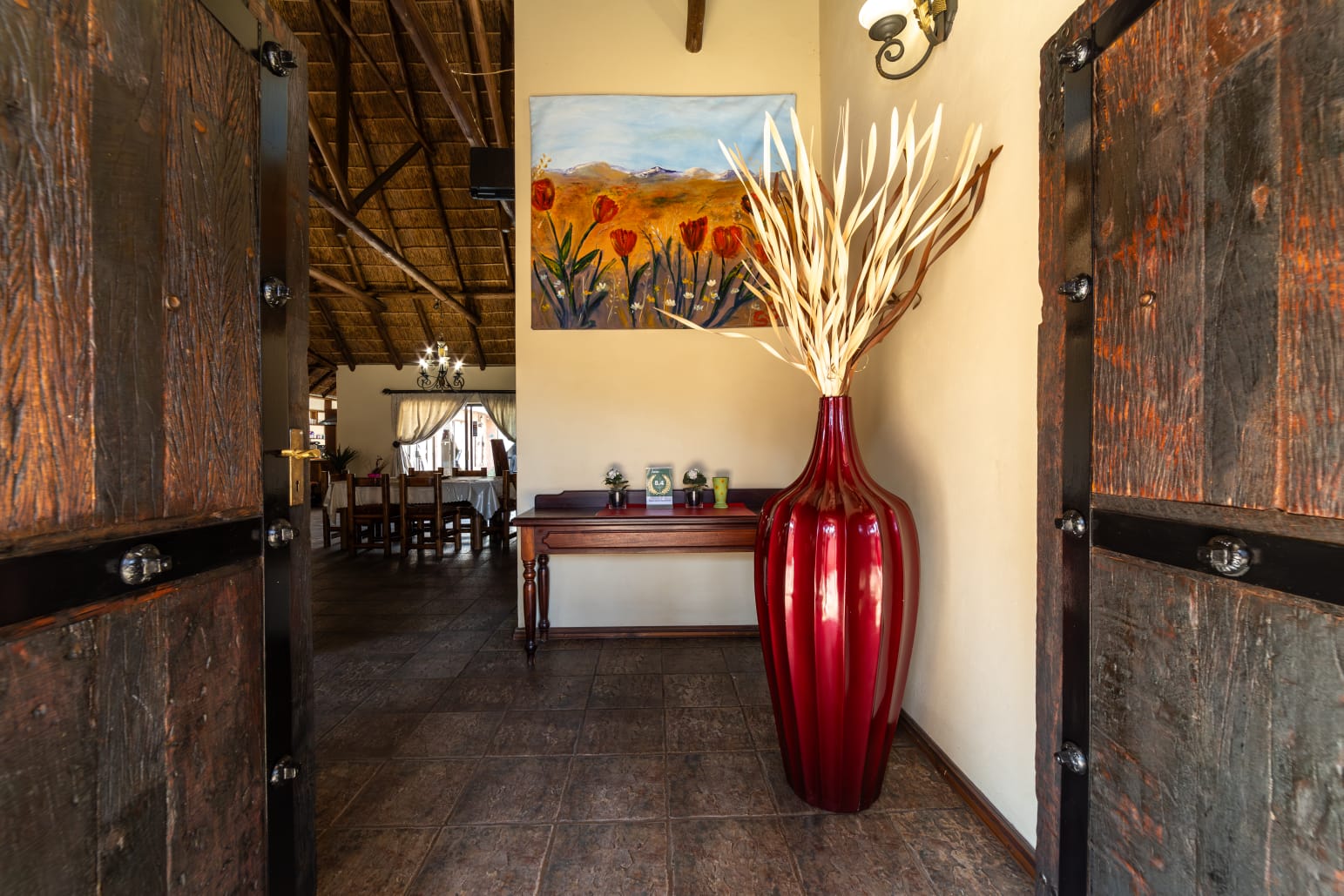 Elegant entrance of Thatch Haven Guesthouse in Eldoraigne featuring a large decorative red vase and traditional thatch roof interior.